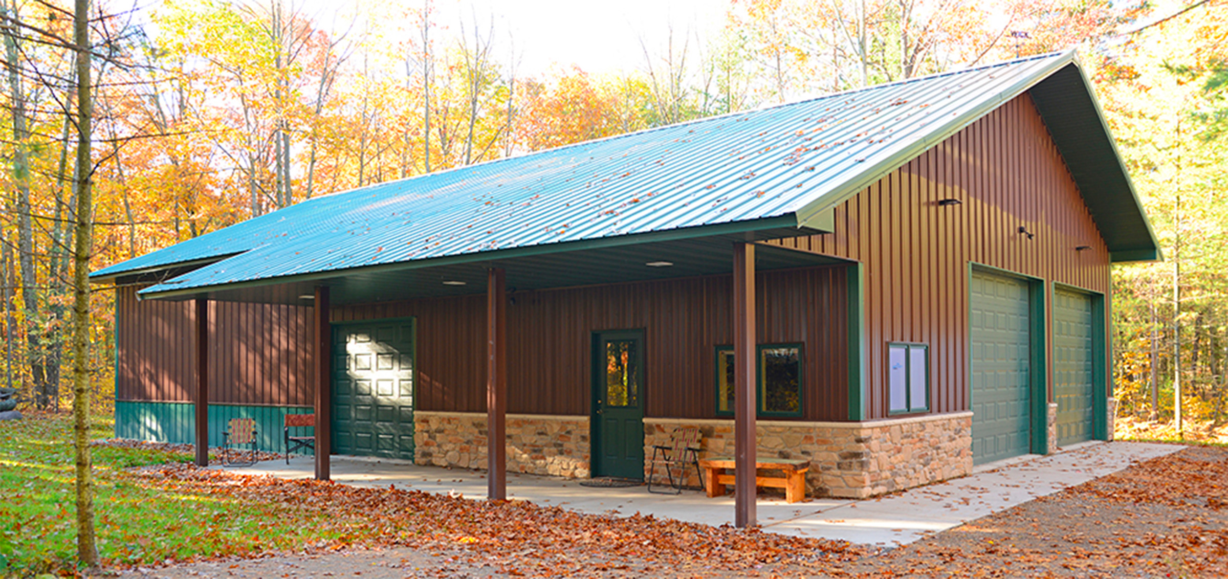 brown and green post frame suburban building surrounded by forest in the fall.